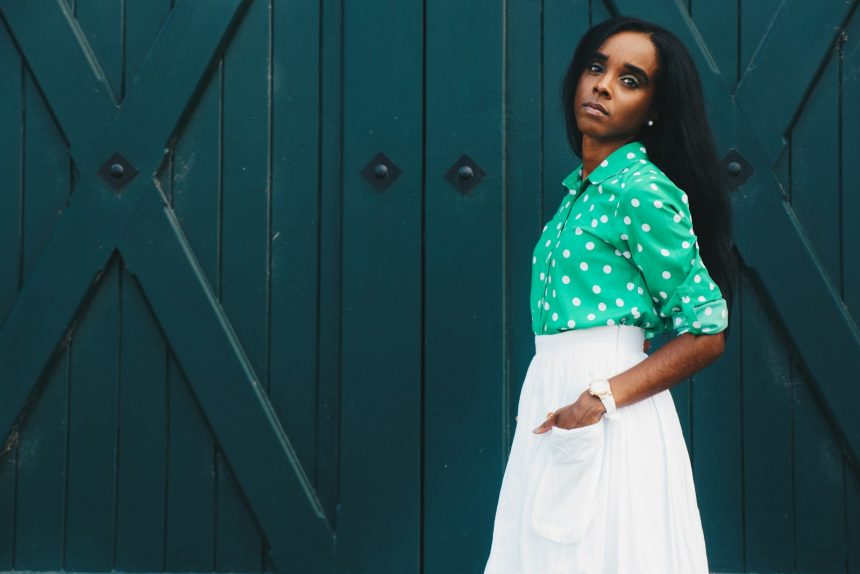 woman in white skirt and green dress shirt hand on pocket standing at the front of green door